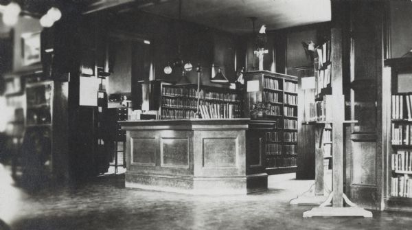 Interior view of the Hudson Public Library. The library opened in 1904 and was funded by Andrew Carnegie with a gift of $12,000. In the foreground is a large librarian's desk, a card catalog, and bookshelves.