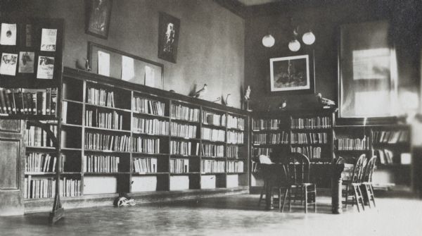 Interior view of the Hudson Public Library. The library opened in 1904 and was funded by Andrew Carnegie with a gift of $12,000. In the room is a children's reading table, and bookshelves lining the walls with stuffed birds displayed on top.