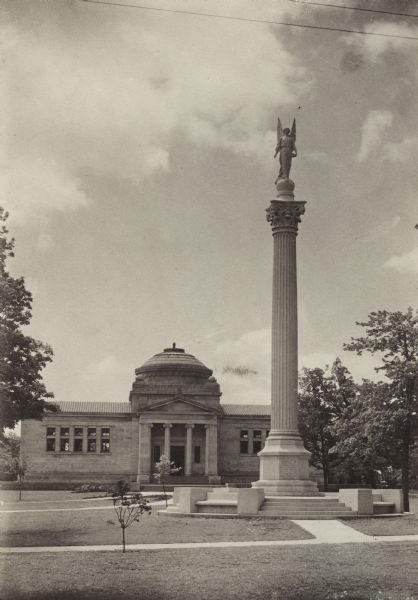 Exterior view of park in front of the Gilbert M. Simmons Public Library, with the Soldiers and Sailors monument. The library opened in 1900 and was funded with a gift of $150,000 from G.M. Simmons.

Atop Soldiers and Sailors monument is the likeness of Nike, the Greek mythological winged goddess of victory.  The figure holds an olive branch in her right hand to symbolize peace, and a laurel wreath in her left hand representing heroism and sacrifice made in war.  The monument honors the Kenosha County men who served in the Union forces of the Civil War.  The monument was dedicated on May 30, 1900.  The Simmons Library opened to the public in July, 1900.