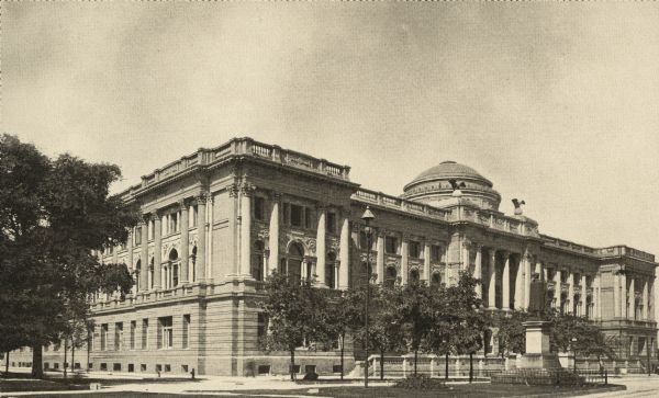 Exterior view of the Milwaukee Public Library. Reverse of the cardboard backing reads: "Milwaukee Public Library and Museum, erected 1898, cost $512,000, Ferry + Clas, Milwaukee, arch." In the foreground is the Washington Monument, and Court of Honor, and in the background is the Milwaukee Public Library and Museum.