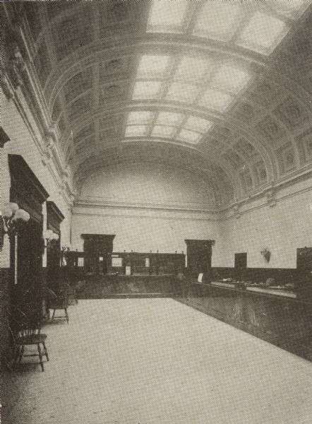 Interior view of the Milwaukee Public Library. Note below the image reads: "Milwaukee Public Library, Delivery Room." There is a vaulted ceiling with skylights, and long marble counters line two of the walls.

