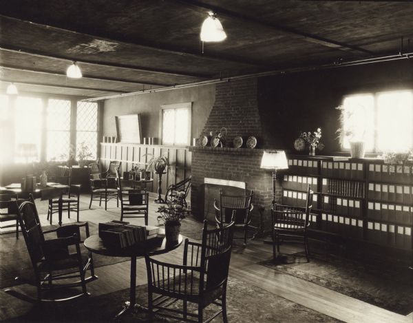 Interior view of the Oconomowoc Public Library. The library was funded by a combined gift of $4,500 from Mrs. Geo Bullen and Mr. P. D. Armour, Sr. Front of photograph reads: "Oconomowoc 1924." Reverse of photograph reads: "Free Library." One section of bookshelves is labeled: "Outlook." Throughout the room are reading tables, chairs, and rocking chairs. Along the back wall is a fireplace flanked by bookshelves. There a lamps in the ceiling, a floor lamp, and large windows along the left wall.