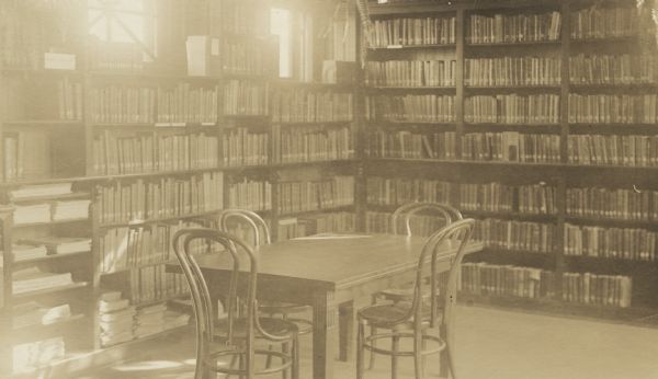 Interior view of the Stanley Public Library. The library opened in 1901 and was funded with a $15,000 donation from Mrs. S.F. Moon. Reverse of the cardboard backing reads: "D.R. Moon Memorial, cost $15,00. - W.C. Whitney, Minneapolis, arch." A reading table with bentwood chairs is in the foreground. Bookshelves line the walls.