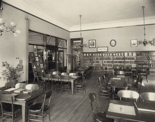 Interior view of the Superior Public Library. In the room are reading tables and bookshelves along the wall. Several doors lead to other rooms, and there is a display of Swiss canton shields.