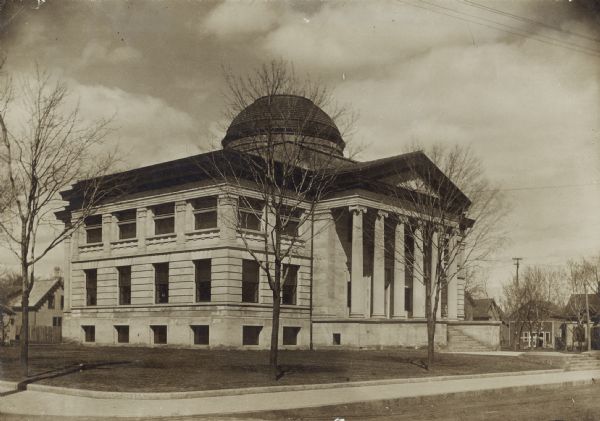 Exterior of Oshkosh Public Library. The entrance has six columns and a pediment at the top of a set of steps, and there is a dome on the roof. Reverse of cardboard backing reads: "$56,500."