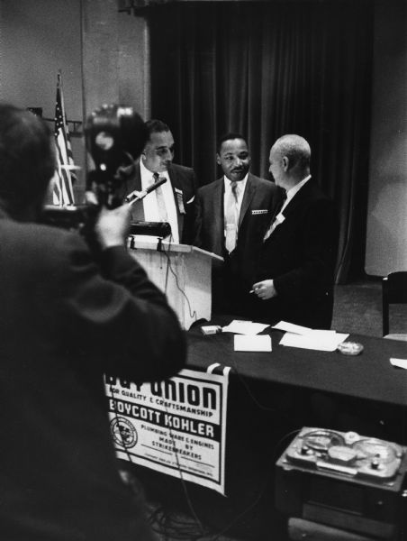 Martin Luther King, Jr., during his appearance at the United Packinghouse Workers of American Wage-Policy Conference.  With him are Russell Lasley (left), a UPWA vice-president, and president Ralph Helstein. A poster at the head table calls attention to the boycott supporting workers on strike against the Kohler Company since 1954.