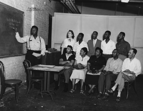 The training school for stewards sponsored by Local 56 of the United Packinghouse Workers of America.  At the blackboard is Otis L. Simmons, the local president.  The man in the back row, on the extreme right, is identified as Roy Gayles.