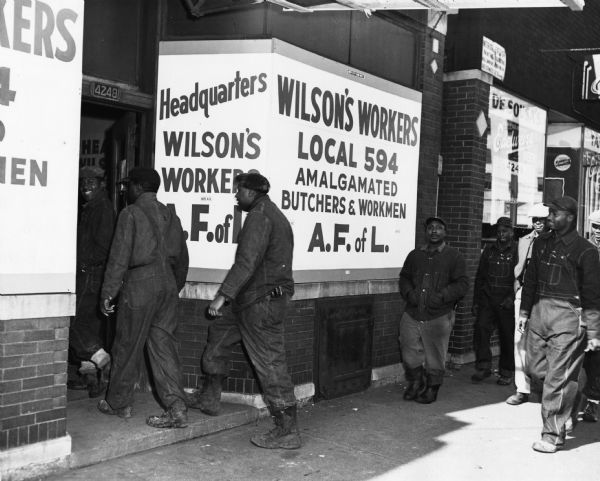 Exterior view of men walking into the Chicago headquarters of the Amalgamated Meatcutters and Butcher Workers Local 594, all employees of the Wilson Packing Company.