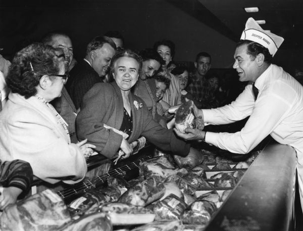 Actor Ernest Borgnine, who was nominated for an Academy Award for his role as a butcher in "Marty", reenacted his role for a publicity photograph at a grocery store opening. Although he tries hard to sell a roast to a customer, the woman appears more interested in having her photograph taken. Borgnine did win the award for his performance.     

