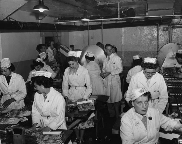 Workers at an Armour plant package bacon for the market. In addition to their hats that say "Anytime is turkey time," the women are all wearing their Amalgamated Meatcutters Union buttons. The operation was being filmed for television.