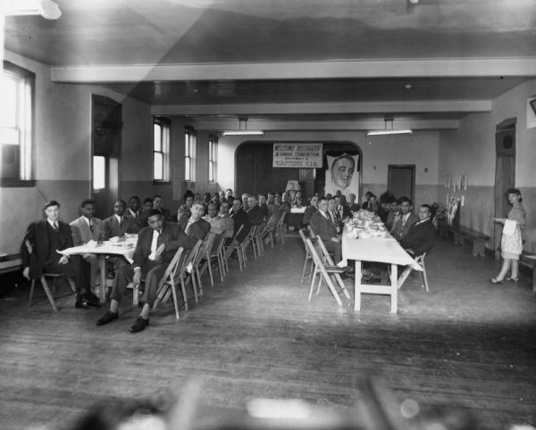 An undated photograph of a convention of District 1 of the United Packinghouse Workers of America. A sign in the background bears a picture of President Franklin D. Roosevet. Another indicates that it is the district's 4th annual convention. The UPWA name was not adopted until 1942, so the photograph probably dates after 1942 although it seems likely the district is including their history under the PWOC (Packinghouse Workers Organizing Committee) in calculating their 4th anniversary.