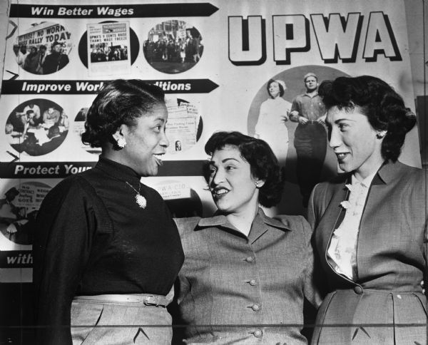 Delegates to the first Women's Activities Conference sponsored by the United Packinghouse Workers of America. A sign behind the three women concerns the importance of labor unions for women.