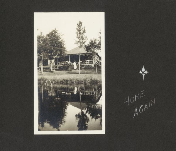 View of Frank and Lillian Drew's cottage on Lake Flora Dell. Their daughter, Delia Drew King, is on the steps. "Home Again" is written along the right side.