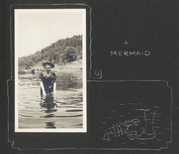 Delia Drew King wades in Lake Flora Dell. There is a hill and shoreline in the background, and a group of people stands near a pier behind Delia. A hand-drawn decorative border, including the caption "A Mermaid," and a cartoon of a lobster about to pinch a human foot underwater accompanies the photograph.