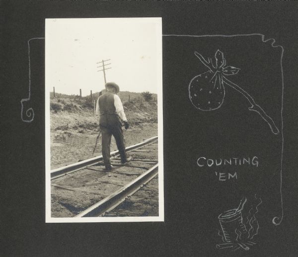 Frank Drew (Frank King's father-in-law) walking railroad tracks. He was known as a prominent banker in the Tomah, Wisconsin community. A hand-drawn decorative border accompanies the photograph in addition to the caption "counting 'em." There is also a drawing of a can cooking over a fire and a handkerchief bundle on a stick.