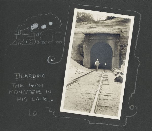 Frank Drew walks a set of railroad tracks near the entrance into a tunnel. The other end of the tunnel can be seen in the distance. A hand-drawn border features a locomotive and railroad cars, and reads, "Bearding the iron monster in his lair."
