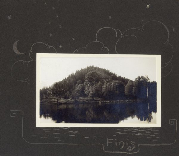 View from lake of the bluff along shoreline of Lake Flora Dell. There is a hand-drawn decorative border, moon, stars and clouds, and the word "Finis."