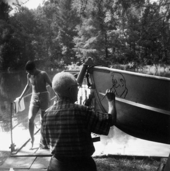 Frank O. King paints his character "Uncle Walt" onto a rowboat. The boy in the background on a pier is King's grand-nephew David Witt Nye.