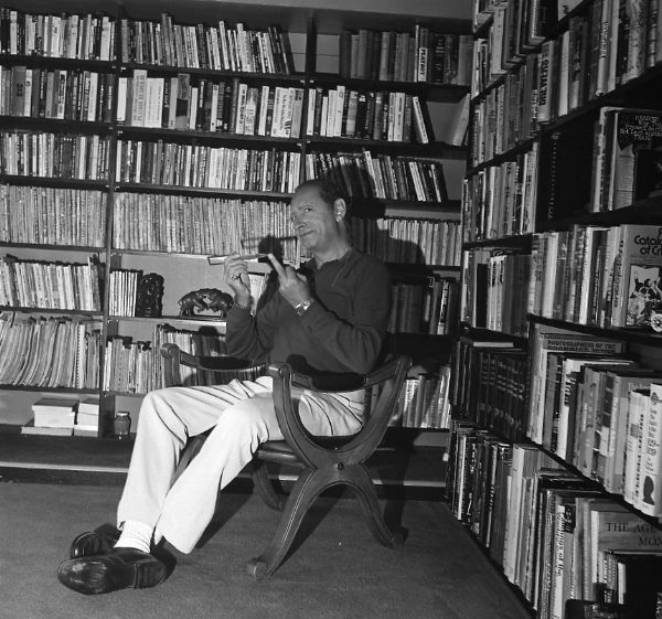 Bloch in his home library in Los Angeles holding a letter opener while making an obscene gesture to the photographer.