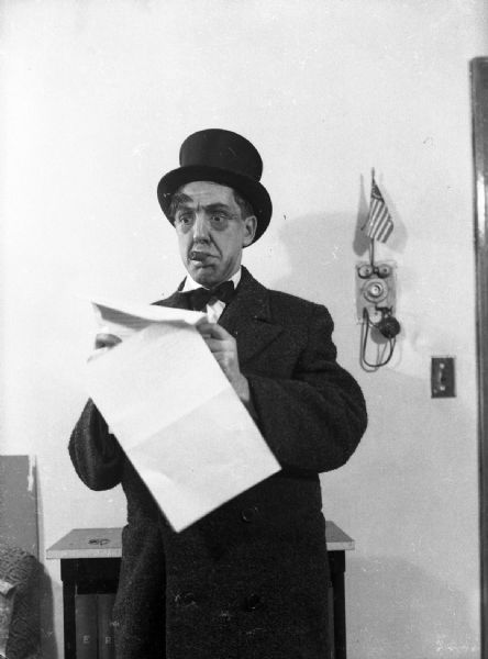 Gauer as a political player. He is wearing a top hat, holding papers smoking a cigar, and gesturing with his left hand. This photograph was meant to illustrate a book on political "types." Similar to Bloch's character photo-illustration. On the wall behind Gauer a small American flag is propped on the apartment intercom.