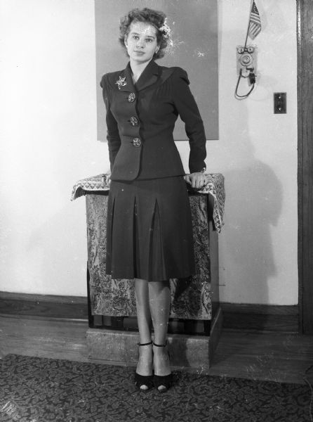 Formal portrait of Angie Vail (nee Siajn), taken by Harold Gauer in his Brady Street apartment. On the wall a small American flag is propped on the apartment intercom.