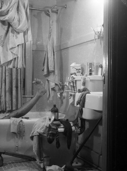 A photograph of a "classy" bathroom that was most likely used in either <i>Cheese</i> or <i>Smiles</i> humor magazine to which Harlod Gauer contributed. There are clothes strewn about, items piled on the toilet, a cigar on the edge of the bathtub, and a fumigating pump is on the floor. A man's leg is visible rising out of the bathtub, most likely belonging to Gauer or Robert Bloch.