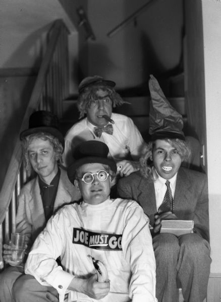 Harold Gauer (wearing a hat, wig, bow tie and smoking a cigar), and three friends, Ed Sachs (who took over the editorship of the Sauk City newspaper), D. Reed Ross (wearing a "Joe Must Go" bumper sticker and holding a banana), and an unknown man who was the editor of the <i>CIO Labor Paper</i>.