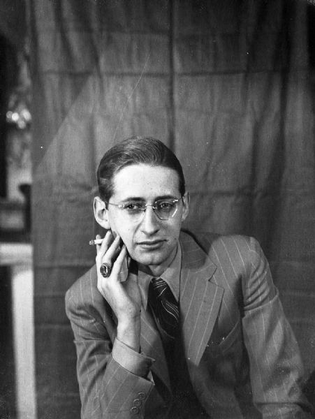 Robert Bloch, wearing a suit and tie, is posed with a cigarette in his right hand.