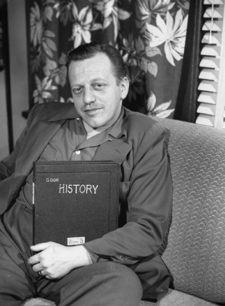 An unknown man is posed on a couch holding a book that has been renamed "Goon History, Volume 3."