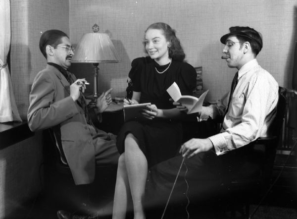Harold Gauer and Robert Bloch, both smoking, pose humorously with an unidentified woman who holds a notepad and pen.