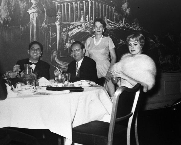 Robert Bloch (wearing eyeglasses), the author of Psycho, sitting at a table with Janet Leigh. His wife Marion Bloch stands behind him. The man in the bow tie is unidentified. This is likely an event related to the 1960 Alfred Hitchcock film Psycho, which was based on the novel by Bloch and starred Leigh.