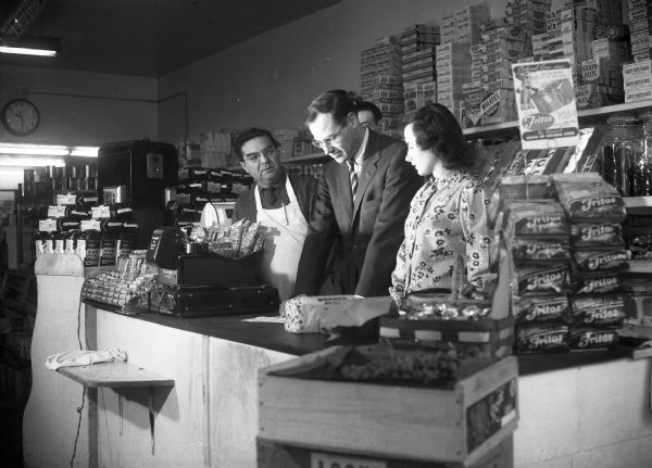 A campaign picture of Democrat Henry Reuss wearing a suit, addressing constituents working at a grocery store. This was likely taken in 1952 while Reuss was running against then-Senator Joe McCarthy.