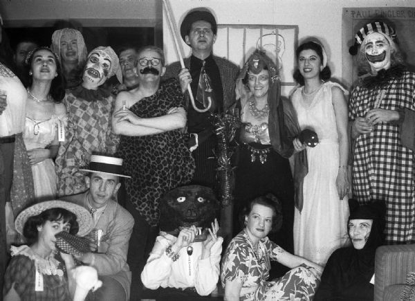 A group portrait of various costumed party attendees, including Chester Vonier (night editor at the <i>Milwaukee Sentinel</i>, wearing strongman garb and fake moustache), Dorothy Madle (reporter for the <i>Milwaukee Sentinel</i>, in black at the bottom right), Robert Bloch (center, with cane) and Alice Bedard (seated, wearing floral print dress).