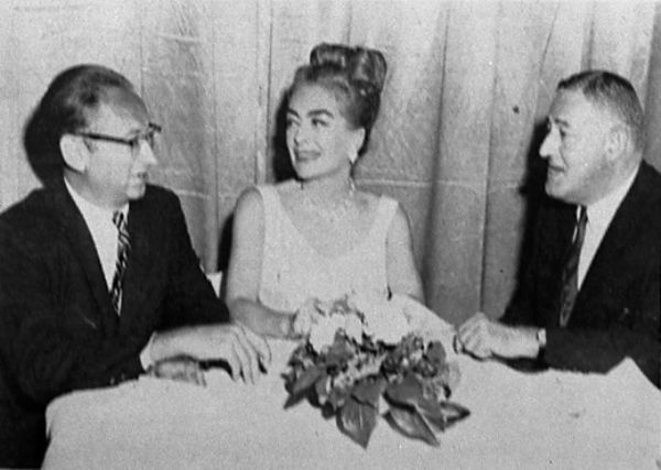 Clipping from a movie magazine of Robert Bloch sitting at a reception table with Joan Crawford and William Castle. The text with the clipping reads "Joan Crawford is flanked by Robert Bloch, left, writer, and William Castle, producer-director, at Columbia's reception honoring the actress on the start of <i>Strait-Jacket</i> which Castle is making for Columbia release." "Motion Picture Herald, August 7, 1963."