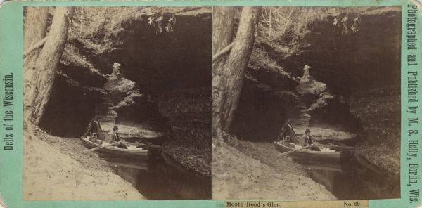 A man rows a small boat through Mouth Rood's Glen. Behind the boat a portable darkroom tent is set up.