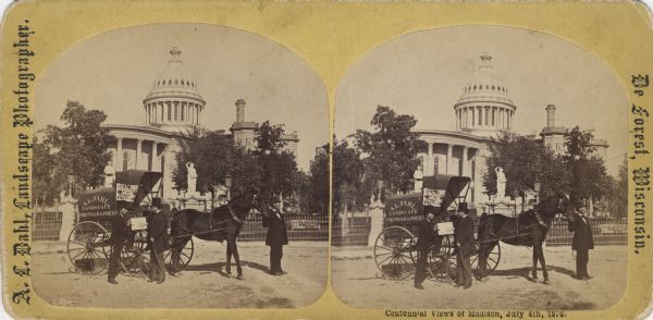 Two men stand by a wagon on which is written "A.L. Dahl Landscape Photographer." The photographer stands on the left side of the view. The flag on the side of Dahl's wagon is a souvenir of the Philadelphia Centennial International Exhibition of 1876. A wrought iron fence surrounds the Capitol Park. This Wisconsin State Capitol building, viewed from West Washington Avenue, was erected in 1857 and replaced in 1913. Caption on stereograph reads, "Centennial Views of Madison, July 4, 1876."