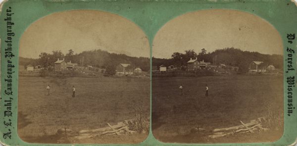 Two men standing in a open field with a farm in the near background. Other people are standing on a hill between the house and barn.