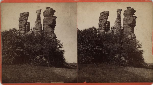 Three men stand atop a large rock formation. Caption on back of stereograph reads, "Three Chimneys 3 miles S. of Viroqua, Wis."