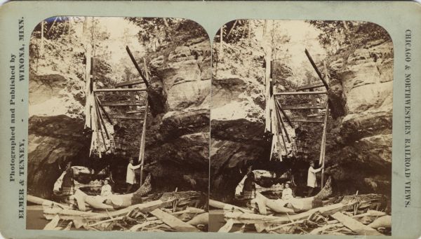 Two women and a man boat through a narrow passageway amidst large rock formations. Wooden debris from an unknown cause blocks their passage. This may be Pewit's Nest, identified on back of stereograph as "Pee-wee's Nest." The people probably arrived by foot since the stream is deep in the gorge but not deep enough for canoeing outside of it.