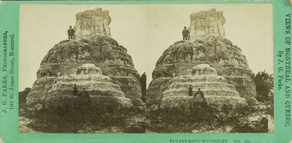 A man, woman, and child stand near or on the Pulpit Rock formation. The man is standing near the top, while the woman and child are near the ground.