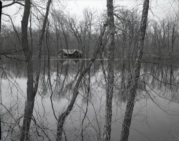 View through trees and over water of a small house in a wooded area surrounded by water due to the flooding of the Wisconsin River.