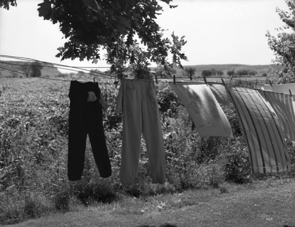 Laundry hangs on a clothesline and blows in the wind. There are fields behind, and low hills in the distance.