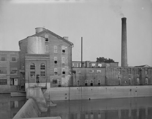 View of a woolen mill, as seen from across a river and dam.
