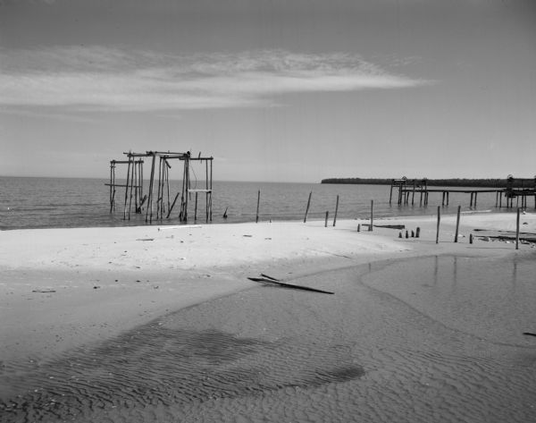 View of the remaining framework of an old fish-unloading track on the Lake Michigan shoreline. A wooded shoreline is beyond a pier in the far background.