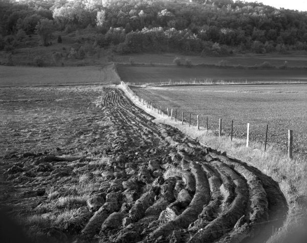View down valley of newly plowed field at the juncture of two fence lines. The farmland belongs to Mr. Carl Meier. A tree-filled ridge is visible in the background.