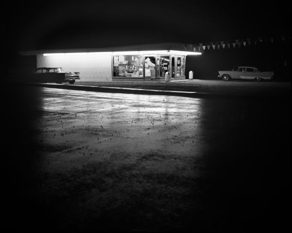 View from across street of Dairy Queen refreshment stand at nighttime. Two cars are visible outside the building.