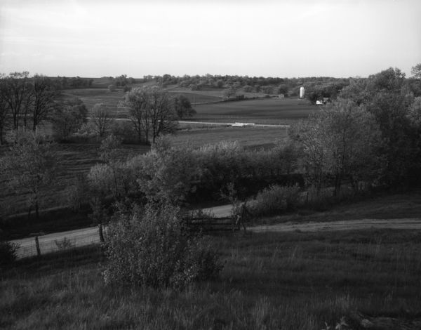 Landscape view of a rolling countryside. A farm is visible in the distance.