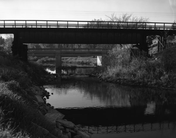 View from river bank of a railroad and a highway bridge crossing the Suamico River.