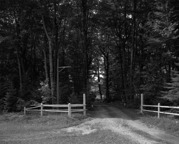 Tree-lined entrance to the D.S. Funk property, which is visible through the trees. Two rustic fences and a lamppost flank the driveway. A sign hanging above the driveway says "Private Road."