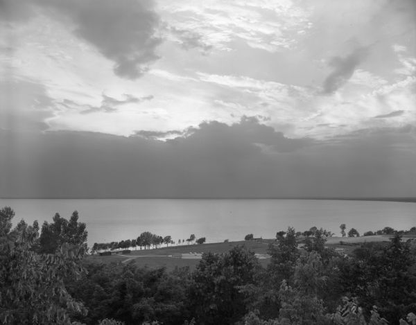 Elevated view of the northern end of Lake Winnebago, seen from High Cliff State Park. The sunset is subdued by a large cloud formation over the lake. On the shoreline, a small pavilion is visible.